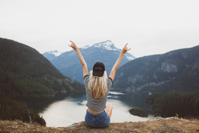 woman sitting on cliff raising both hands